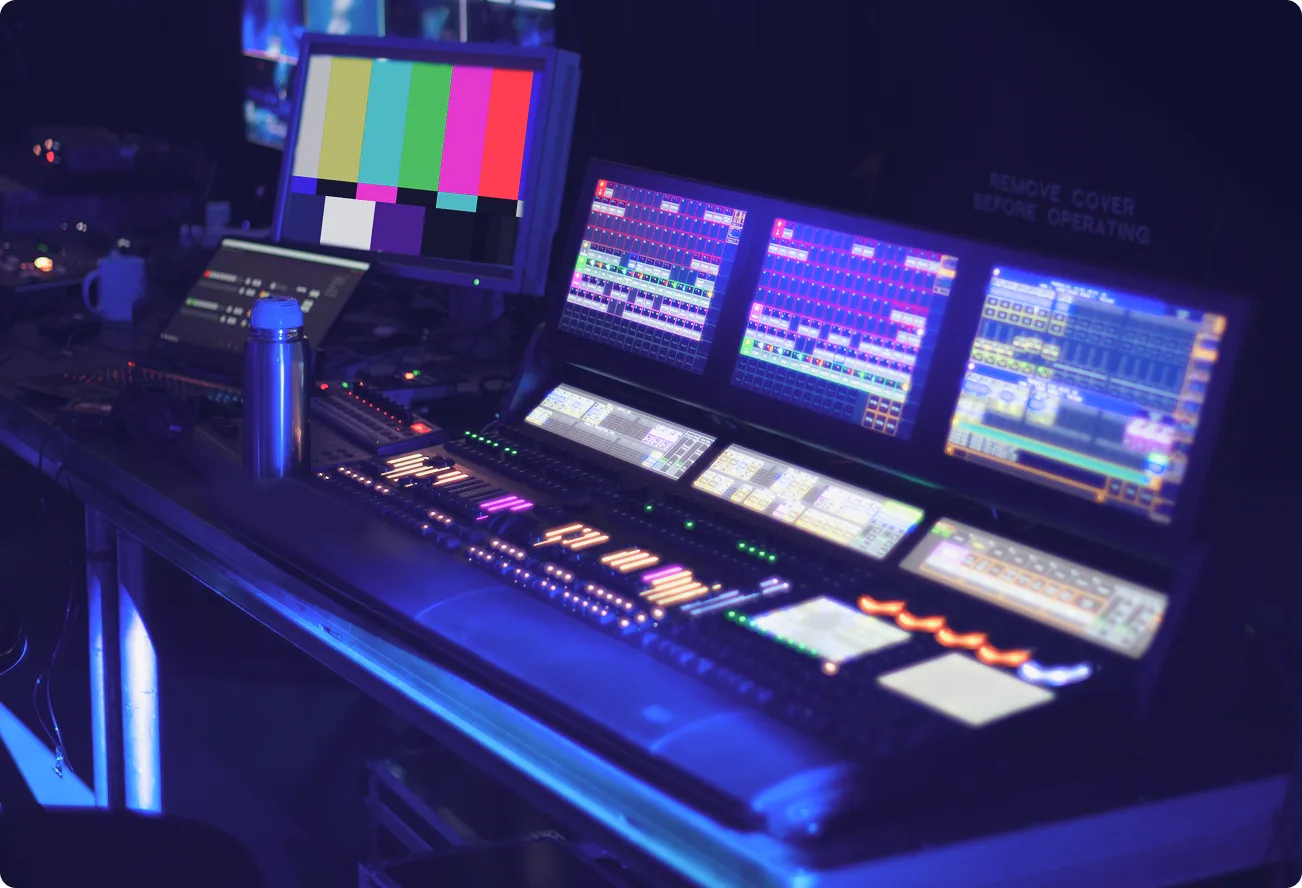 Concert control desk with multiple monitors and LED-lit mixing console.